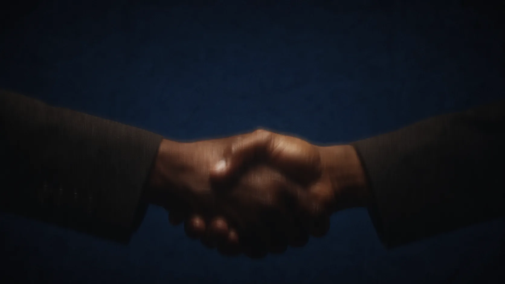 Two people shaking hands, lit against a dark blue ground.